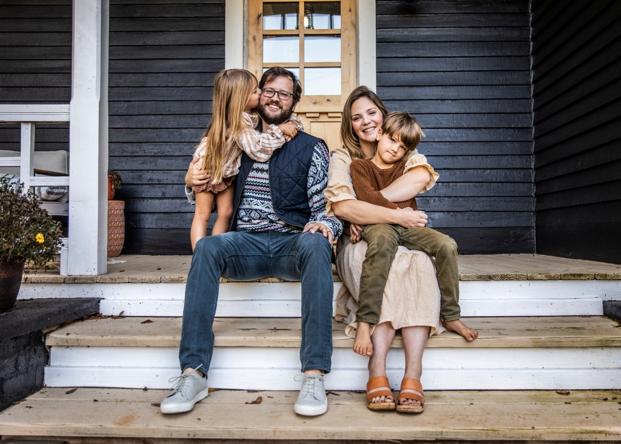 Husband and wife sitting on the front porch with their two kids